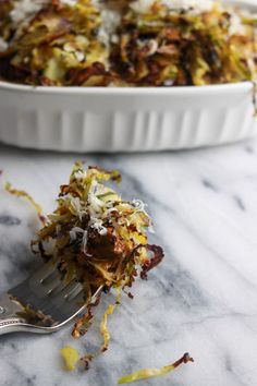 a close up of a fork with food in it on a marble counter top next to a casserole dish