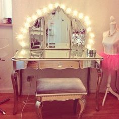 a dressing table with a mirror, stool and lights on it in front of a chair