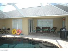 a house with a pool and chairs in the back yard next to an enclosed patio