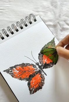 a drawing of a butterfly being held up by someone's hand on top of a white sheet