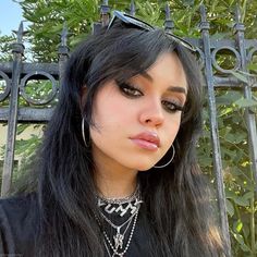 a woman with long black hair and large hoop earrings is looking at the camera while standing in front of a gate