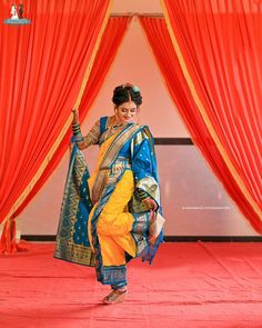 a woman in a yellow and blue sari is walking through an orange stage with red drapes