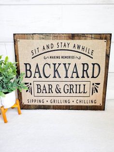 a sign that says backyard bar and grill sitting next to a small potted plant