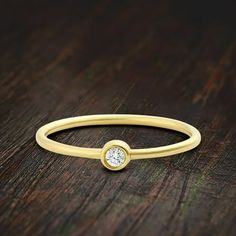 a yellow gold ring with a single diamond on the top, sitting on a wooden surface