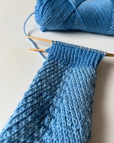 two knitting needles are next to a blue knitted sock and ball of yarn on a white surface