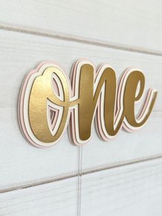 the word'one'is painted in gold and silver on a white wall with wood slats