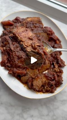 a white plate topped with meat covered in gravy next to a glass window