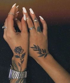 two hands with tattoos and rings on their fingers, one holding the other's hand