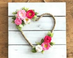 a heart shaped sign with flowers hanging from it's side on a wooden table