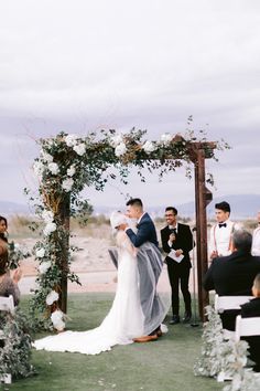 a bride and groom are kissing under an arch with flowers on it at their wedding ceremony