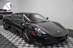 a black sports car is parked in a garage with two other cars behind it on a checkered floor