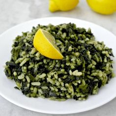 a white plate topped with green rice and lemons next to two lemon wedges