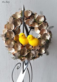 two yellow birds sitting on top of a metal stand next to shells and flowers in the shape of a wreath