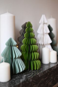 some paper christmas trees on a mantle with candles in front of them and one is green