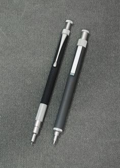 two pens sitting next to each other on top of a gray cloth covered flooring