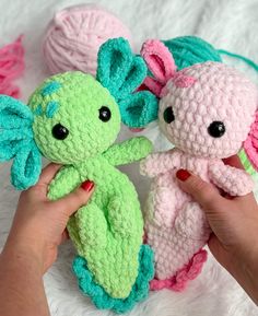 two crocheted stuffed animals being held by someone's hand on a white blanket