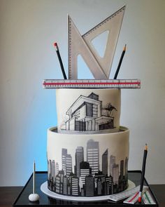 a three tiered cake decorated with cityscape and pencils on top of it