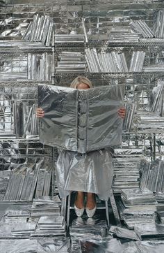 a woman is sitting on a chair covered in silver foil and holding a large piece of material