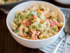 a white bowl filled with pasta salad on top of a wooden table next to silverware