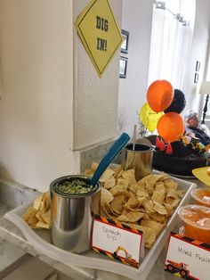 a tray with chips and dips on it next to some orange balloons in the background