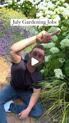 a man sitting on the ground in front of flowers pointing at something with his finger