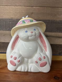 a ceramic rabbit with a straw hat on its head sitting on a wooden table next to a wall