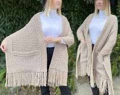 two women standing next to each other wearing knitted shawls with tassels