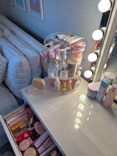 a vanity with makeup and other items on it in front of a mirror that is lit up