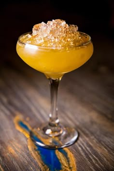 a yellow drink with sugar on top in a coupe glass sitting on a wooden table