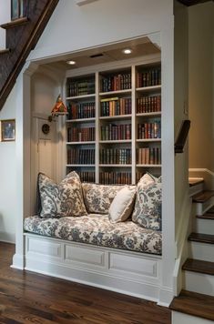 a couch sitting in front of a bookshelf filled with lots of books next to a stair case