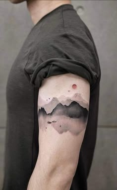 a man with a black and grey mountain tattoo on his arm, showing mountains in the distance