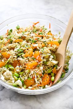 a glass bowl filled with rice, carrots and peas next to a wooden spoon