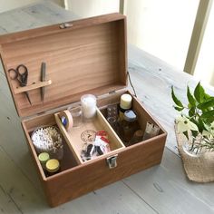 an open wooden box on a table with scissors and other items in it next to a potted plant