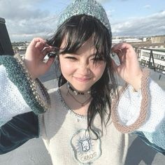 a young woman wearing a knitted hat and holding her hands up to her ears