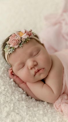 a baby is laying down wearing a pink dress and a flower headband with her eyes closed