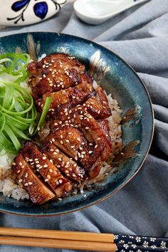 a blue plate topped with meat and rice next to chopsticks