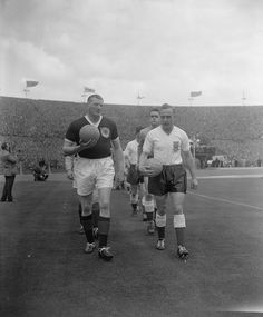 an old photo of two men walking on the field with a ball in their hands