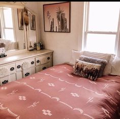 a bed sitting under a window next to a dresser with drawers and pillows on top of it