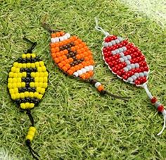 three beaded kites are laying on the grass together, one is orange and one is yellow