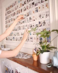 two women are placing pictures on the wall above a table with potted plants in front of them