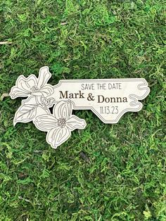 a wooden save the date sign sitting on top of green grass with flowers in it