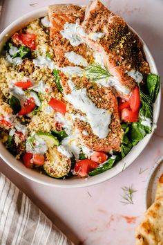 a white bowl filled with salmon and veggies on top of a pink table