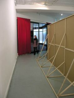 a person walking down a long hallway next to a red curtain and some people in the background