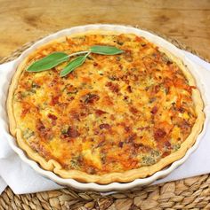 a quiche with cheese and vegetables in a white dish on a wicker basket