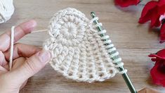 someone is crocheting a piece of yarn on a wooden table with flowers in the background