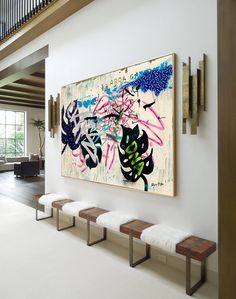 a large painting hanging on the wall next to benches in a room with white walls