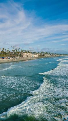 an ocean view with waves crashing on the beach and palm trees lining the shoreline in the background