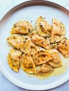 a white plate topped with ravioli covered in cheese and seasoning next to a fork