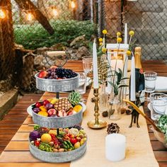 an outdoor table is set with candles, plates and bowls of fruit on the table