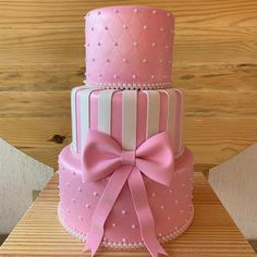 a three tiered cake with pink and white frosting, decorated with a bow